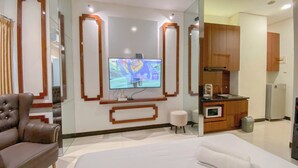 A hotel room with a large bed, a leather armchair, a television mounted on the wall, and a kitchenette area. - Good Choice Studio Apartment At Sentraland Semarang (Semarang)