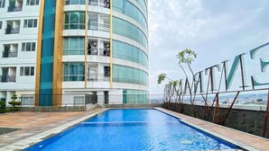 A modern hotel with a curved glass facade, a swimming pool, and a view of the cityscape. - Good Choice Studio Apartment At Sentraland Semarang (Semarang)