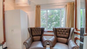 A room with two brown leather armchairs, a white refrigerator, and a window with curtains. - Good Choice Studio Apartment At Sentraland Semarang (Semarang)