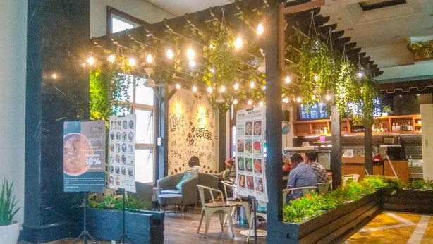 An indoor coffee shop with hanging lights, a menu board, and seating areas. - Comfortable Studio (No Kitchen) At Grand Palace Kemayoran Apartment (Jakarta)