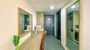 A hotel hallway with a wooden reception desk, a green plant, a mirror, and a door leading to a room. - Comfortable Studio (No Kitchen) At Grand Palace Kemayoran Apartment (Jakarta)
