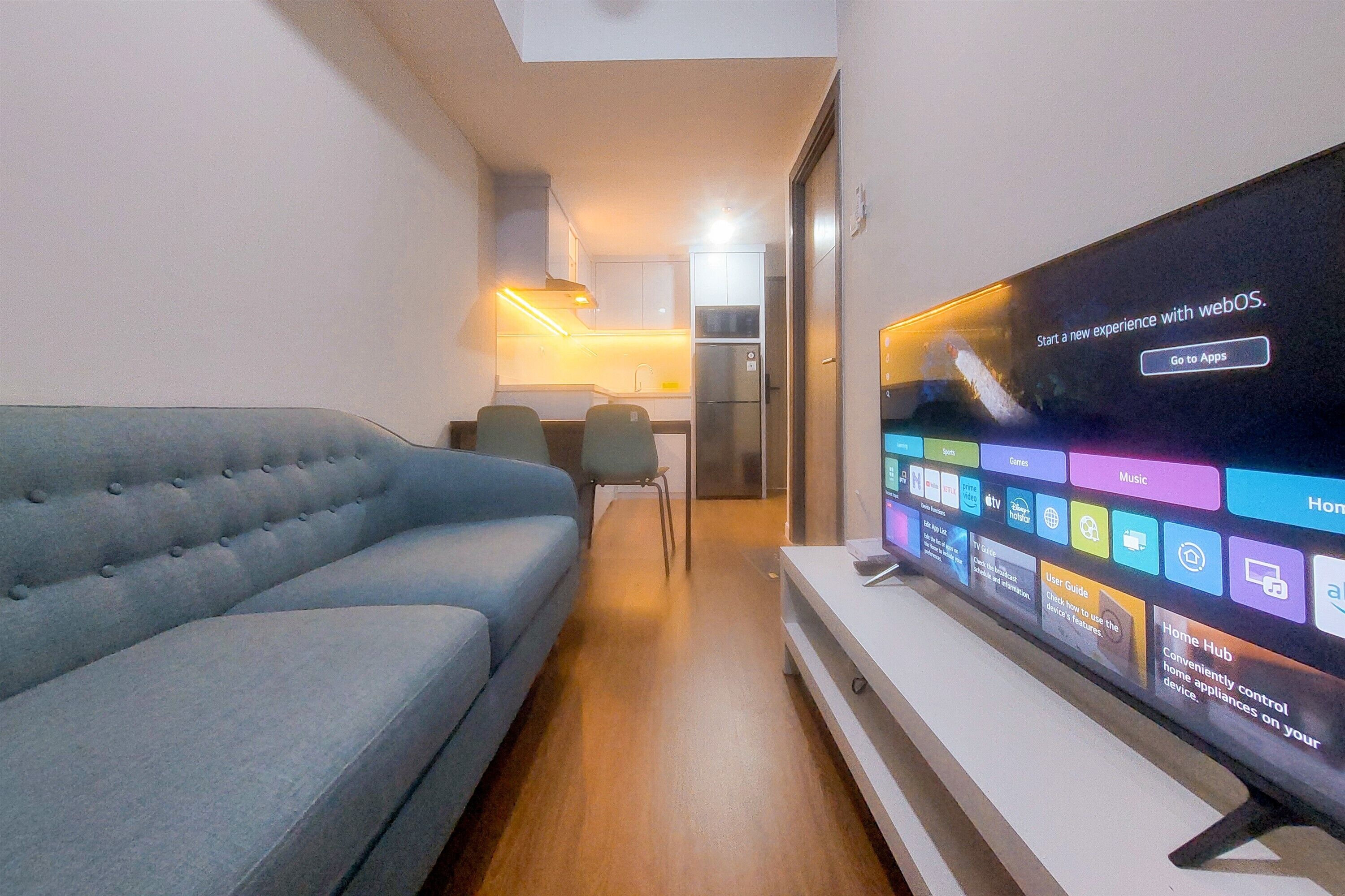 A living room with a large flat-screen TV displaying a home hub interface, a grey sofa, and a wooden floor.