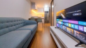 A living room with a large flat-screen TV displaying a home hub interface, a grey sofa, and a wooden floor. - Cozy And Simply 1Br Apartment Anwa Residence (South Tangerang)