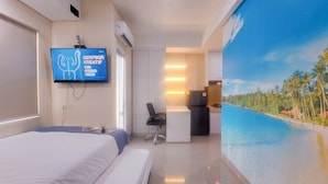 A hotel room with a bed, a desk, a chair, a TV, and a wall mural.