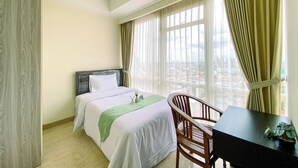 Habitación de hotel con cama, escritorio y silla. Cuenta con ventana con cortinas y vistas a la ciudad.