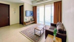 Una sala de estar moderna con un televisor de pantalla plana, un sofá, una mesa de centro y un amplio ventanal con cortinas.