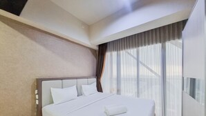A hotel room with a large bed, a headboard, a window with curtains, and a light fixture on the ceiling. - Cozy And Warm Studio Room At Uttara The Icon Apartment (Depok)