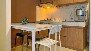 Een compacte keuken met een witte tafel en stoelen, een klein spoelgedeelte en houten kastjes.