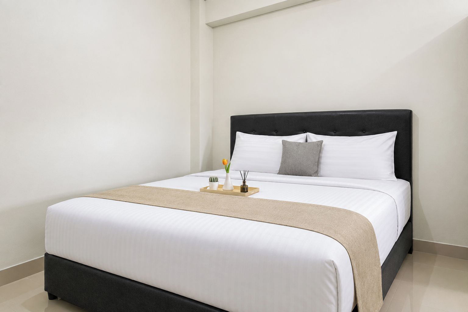 A neatly made bed with white linens, a dark headboard, and a small bedside table with a vase and a tray.