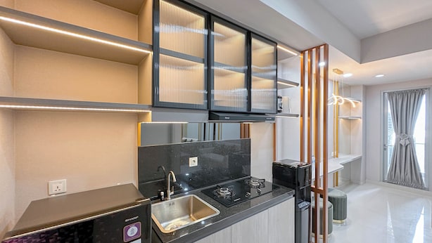 Una cocina moderna con estufa integrada, pileta y encimera negra. Hay alacenas sobre la encimera y una ventana con cortinas.
