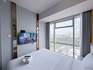 Habitación de hotel con una cama grande, un televisor montado en la pared y vistas a la ciudad a través de un ventanal.