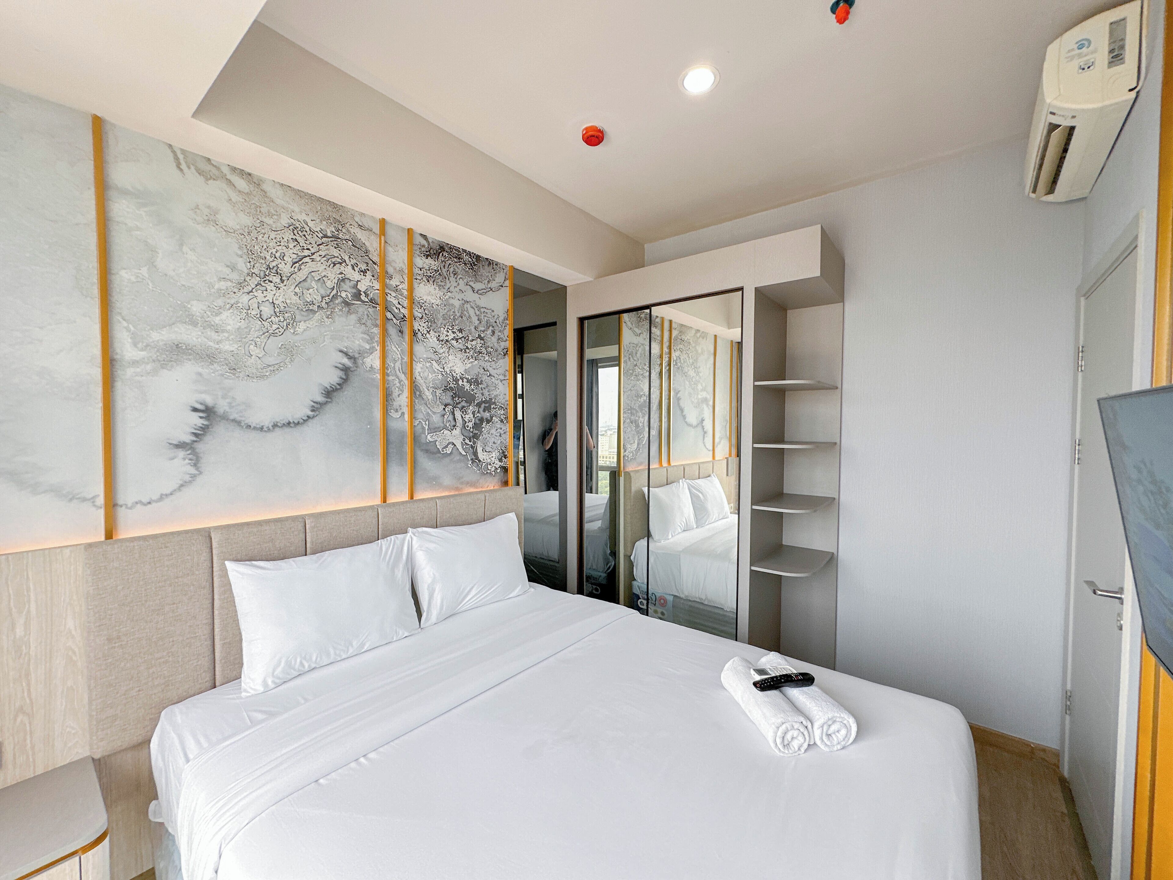 A modern hotel room with a large bed, a wall-mounted artwork, a built-in wardrobe, and a ceiling-mounted air conditioning unit.