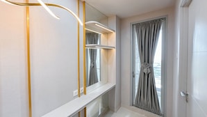 Un baño moderno con un espejo grande, un tocador con detalle dorado y vistas de la ciudad a través de una ventana con cortinas.