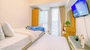A hotel room with two beds, a TV mounted on the wall, a desk with a plant, and a window with curtains. - Serene Studio At 25Th Floor Apartment Tokyo Riverside Pik 2 (Teluknaga)