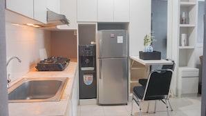 A compact kitchen with a stainless steel refrigerator, a sink, a small countertop, and a chair.