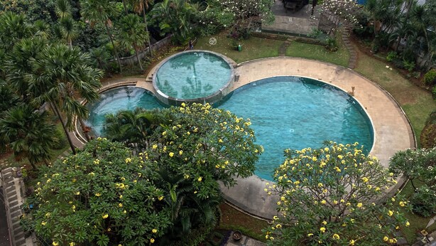 A large outdoor swimming pool surrounded by lush greenery and a small garden area.