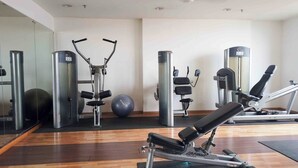 A gym with exercise equipment, a mirrored wall, and a wooden floor.