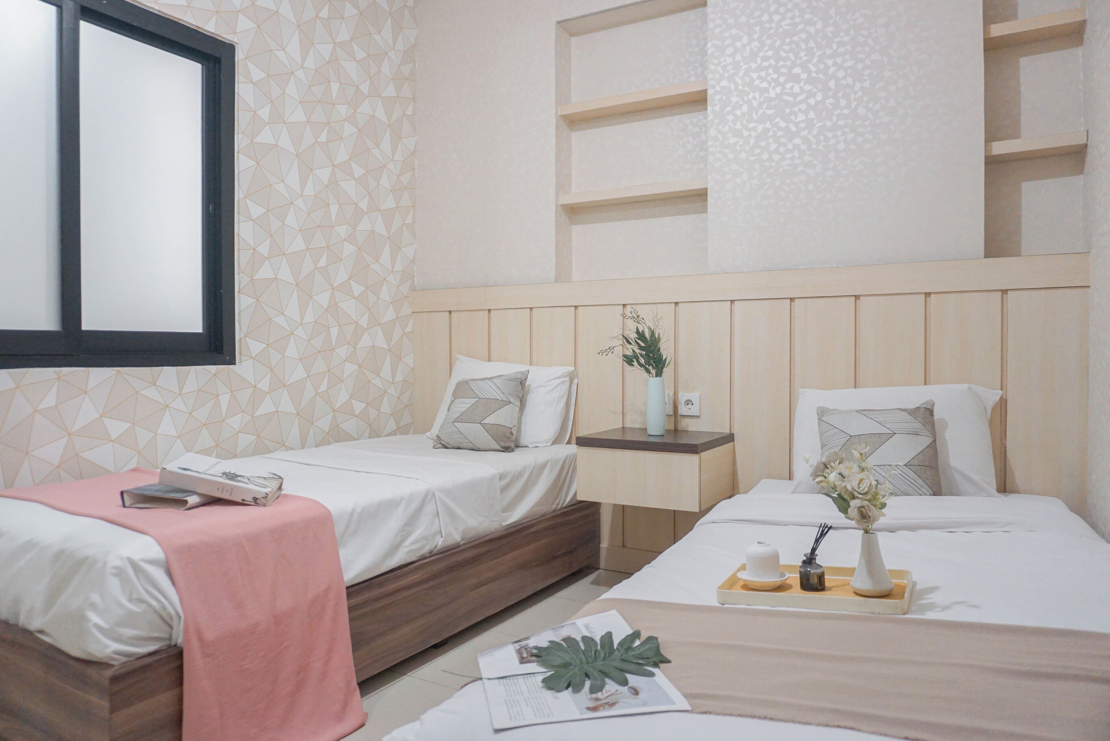 A hotel room with two beds, a wooden headboard, a bedside table with a vase and a tray, and a geometric patterned wall.
