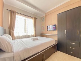 Una habitación de hotel con cama, cortinas, televisor en la pared y armario.