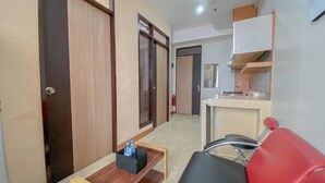 A compact hotel room with a kitchenette, a small table with a bottle holder, and a red chair. - The Chic 2Br Apartment At The Edge Bandung (Cimahi)