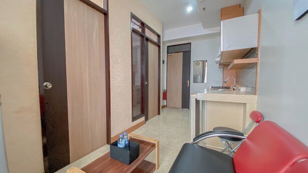 A compact hotel room with a kitchenette, a small table with a bottle holder, and a red chair.