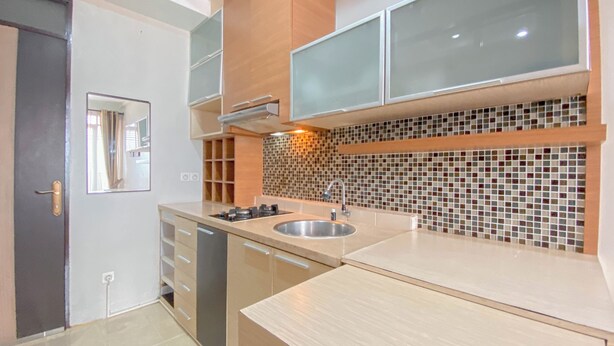 A modern kitchen with a central island, built-in cabinets, and a tiled backsplash. - The Chic 2Br Apartment At The Edge Bandung (Cimahi)