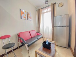 Una sala de estar con un sofá rojo, una mesita de madera, un refrigerador y dos sillas.