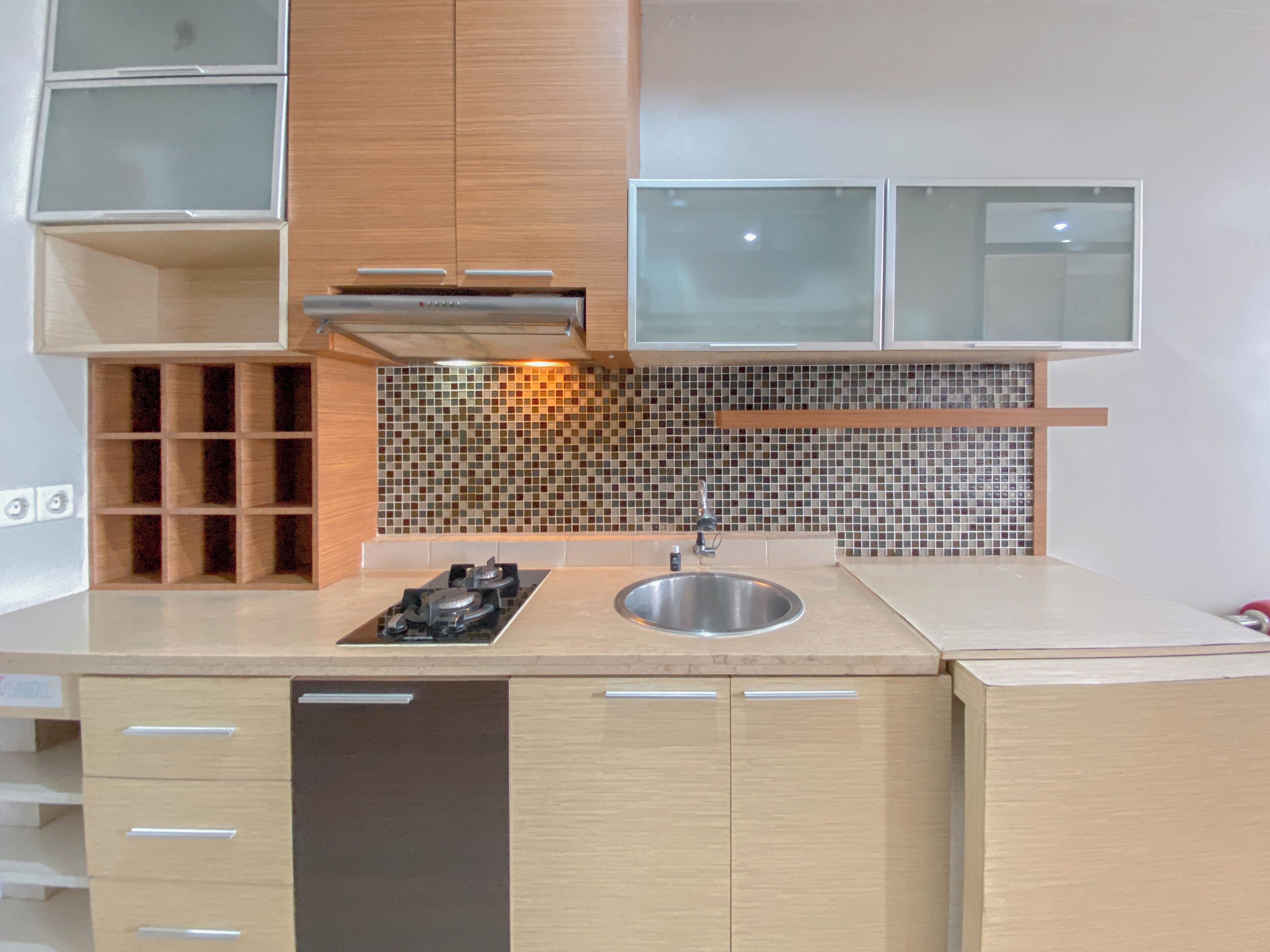 Una cucina moderna con piano cottura a gas, lavello in acciaio inox, mobili in legno e backsplash con piastrelle a mosaico.