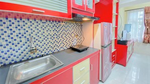 Una cocina con armarios rojos, salpicadero de azulejos, pileta de acero inoxidable y refrigerador rojo.