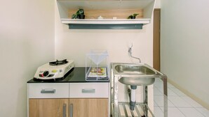 A compact kitchen with wooden cabinets, a countertop with a rice cooker, a sink, and a shelf above the countertop with potted plants.