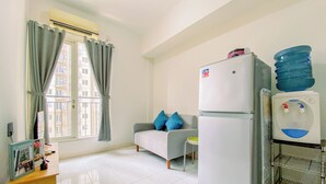 A small, clean room with a kitchenette, a sofa with blue cushions, a small table, and a window with curtains.