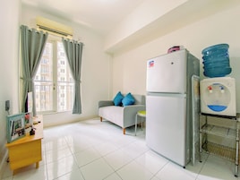 Una habitación pequeña y limpia con kitchenette, un sofá con cojines azules, una mesita y una ventana con cortinas.