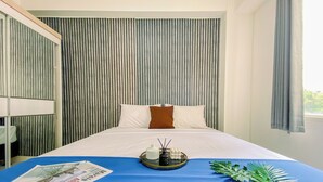 A hotel room with a bed, a blue bedspread, a tray with a plant, and a newspaper.