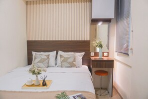 A neatly arranged bedroom with a bed, bedside table, and a small stool. - Warm And Modern Style 2Br At Meikarta Apartment (Cikarang)