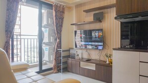 Un salon avec un canapé, un téléviseur à écran plat fixé au mur, un coin cuisine équipé d’une cuisinière et un balcon offrant une vue sur la ville.