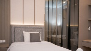 A hotel room with a bed, a grey headboard, a glass partition, and a white towel on the side table. - Cozy 2Br Apartment M-Town Signature (Gading Serpong)