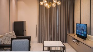 A modern living room with a sofa, a dining table, a flat-screen TV, and a chandelier. - Cozy 2Br Apartment M-Town Signature (Gading Serpong)