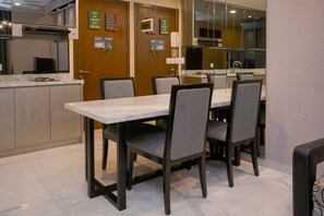 A modern kitchen with a marble countertop, a dining table with four chairs, and a microwave on the wall. - Cozy 2Br Apartment M-Town Signature (Gading Serpong)