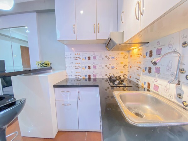 Cocina compacta con armarios blancos, un lavamanos de acero inoxidable y un salpicadero decorado con ilustraciones de alimentos y bebidas.