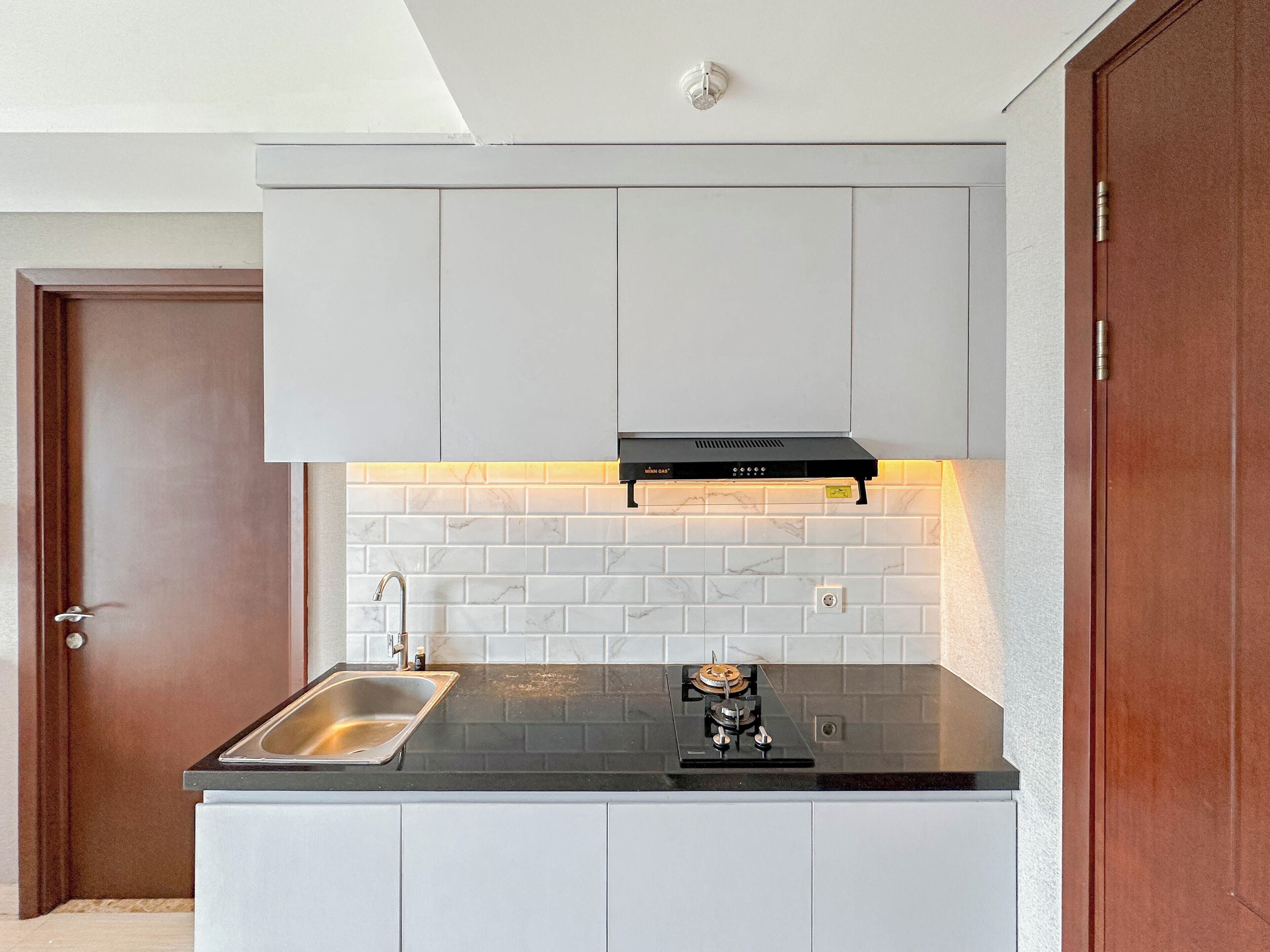 Une cuisine moderne avec des meubles blancs, un plan de travail noir, un évier en acier inoxydable et une cuisinière à gaz.