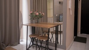 Een gezellig eetgedeelte met een houten tafel, vier krukken, een potplant met roze bloemen en een spiegel aan de muur.