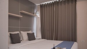 Een moderne hotelkamer met een groot bed, nachtkastje, een wandplank met decoratieve objecten en een raam met gordijnen.