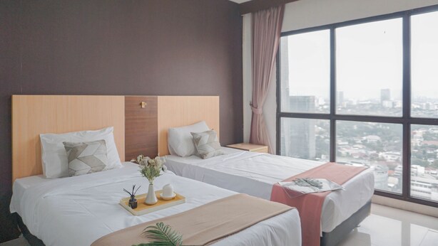 Ein Hotelzimmer mit zwei Betten, einem großen Fenster mit Blick auf die Stadt und einem Tablett mit Blumen und einer Tasse auf dem Bett.