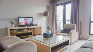 A modern living room with a glass coffee table, beige sofas, a television, and a large window with curtains. - Best Location And Strategic 2Br At Tamansari Semanggi Apartment (Jakarta)