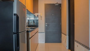 A narrow kitchen with a refrigerator, a sink, and a door. - Comfortable Studio At Tamansari Semanggi Apartment (Jakarta)
