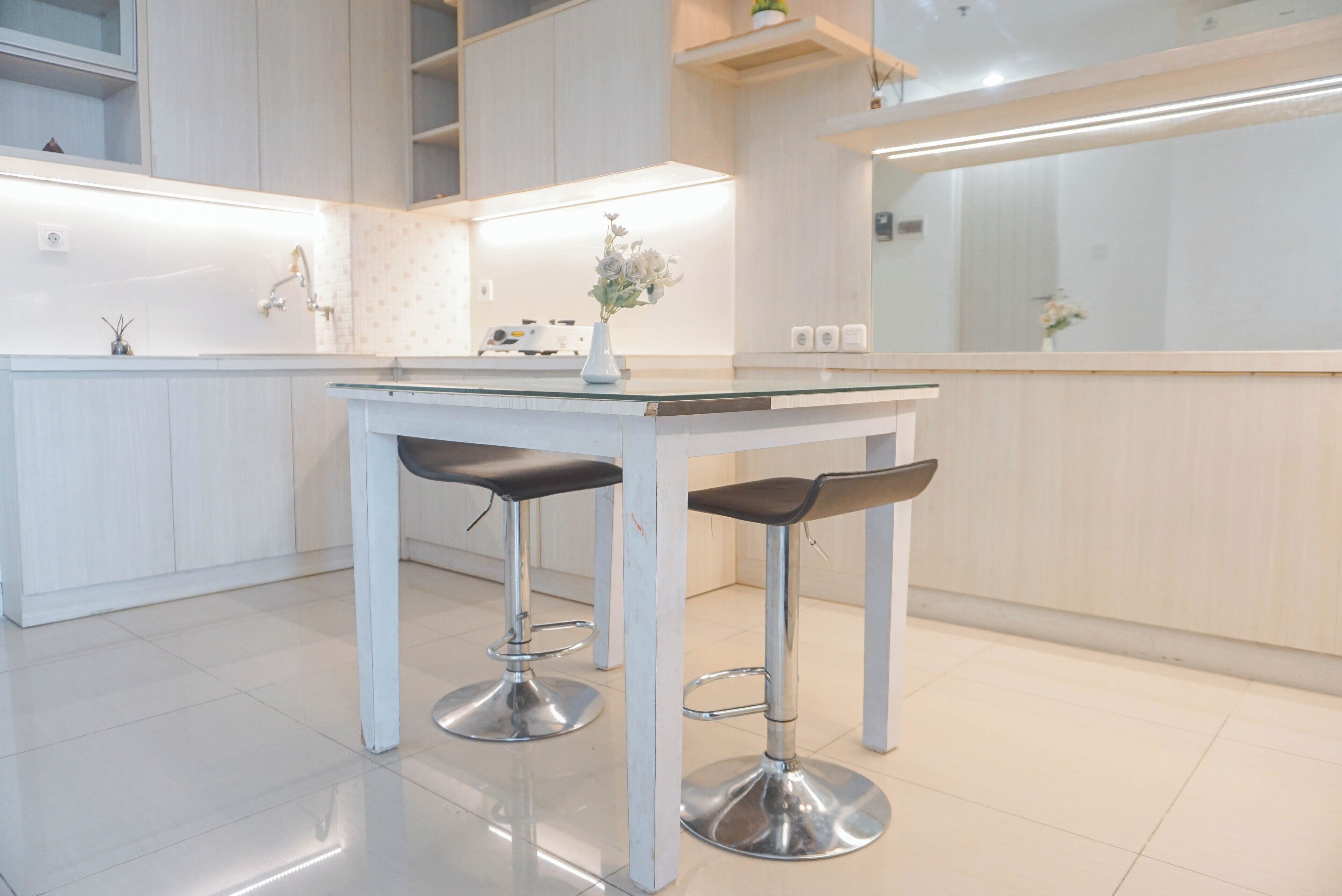 A modern kitchen with white cabinetry, a white countertop, and two bar stools with black seats.