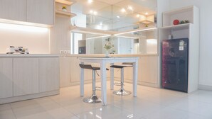 A modern kitchen with white cabinetry, a central island with stools, and a refrigerator. - Comfy And Modern 2Br Grand Kamala Lagoon Apartment (Bekasi)