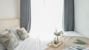 A neatly made bed with geometric patterned pillows, a tray with a vase of flowers, and a magazine on the bed. - Comfy And Modern 2Br Grand Kamala Lagoon Apartment (Bekasi)