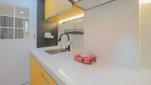 A modern kitchen with white countertops, a red induction cooktop, a black faucet, and a window with curtains. - Homey And Comfortable Studio Apartment At Daan Mogot City (Jakarta)