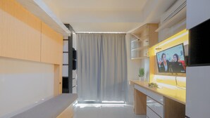 A modern, compact living space with a built-in bench, a flat-screen TV, and a sliding door leading to a balcony. - Homey And Comfortable Studio Apartment At Daan Mogot City (Jakarta)